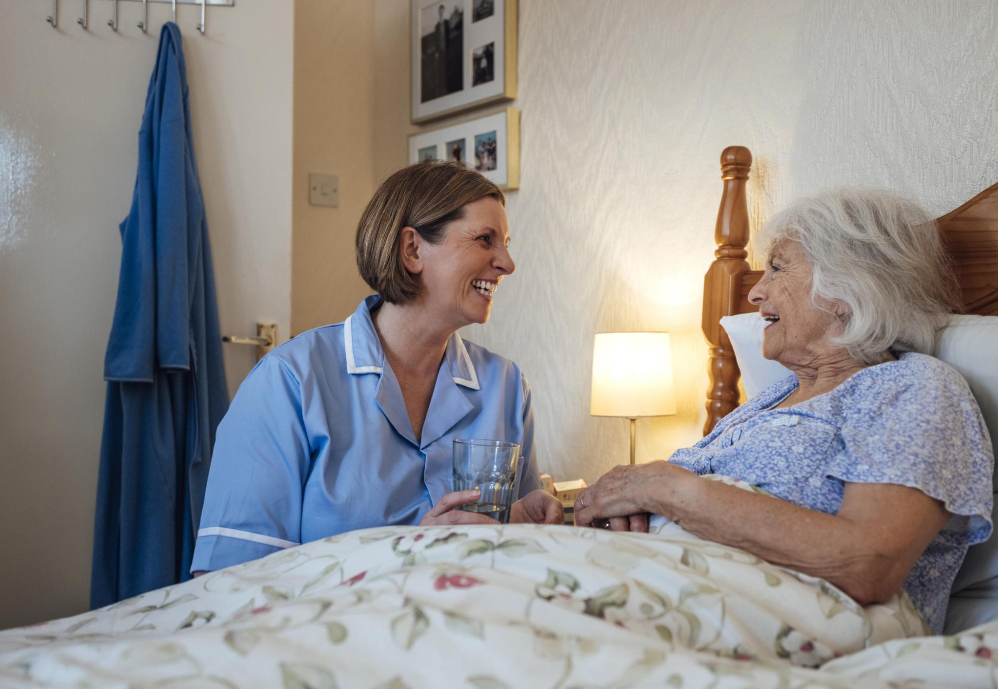 Senior woman lying in bed being helped by a home carer