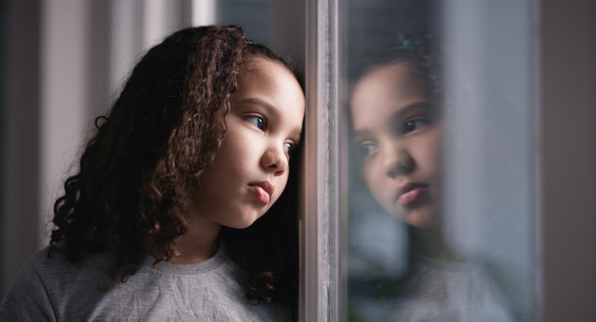 A sad girl looks through a window