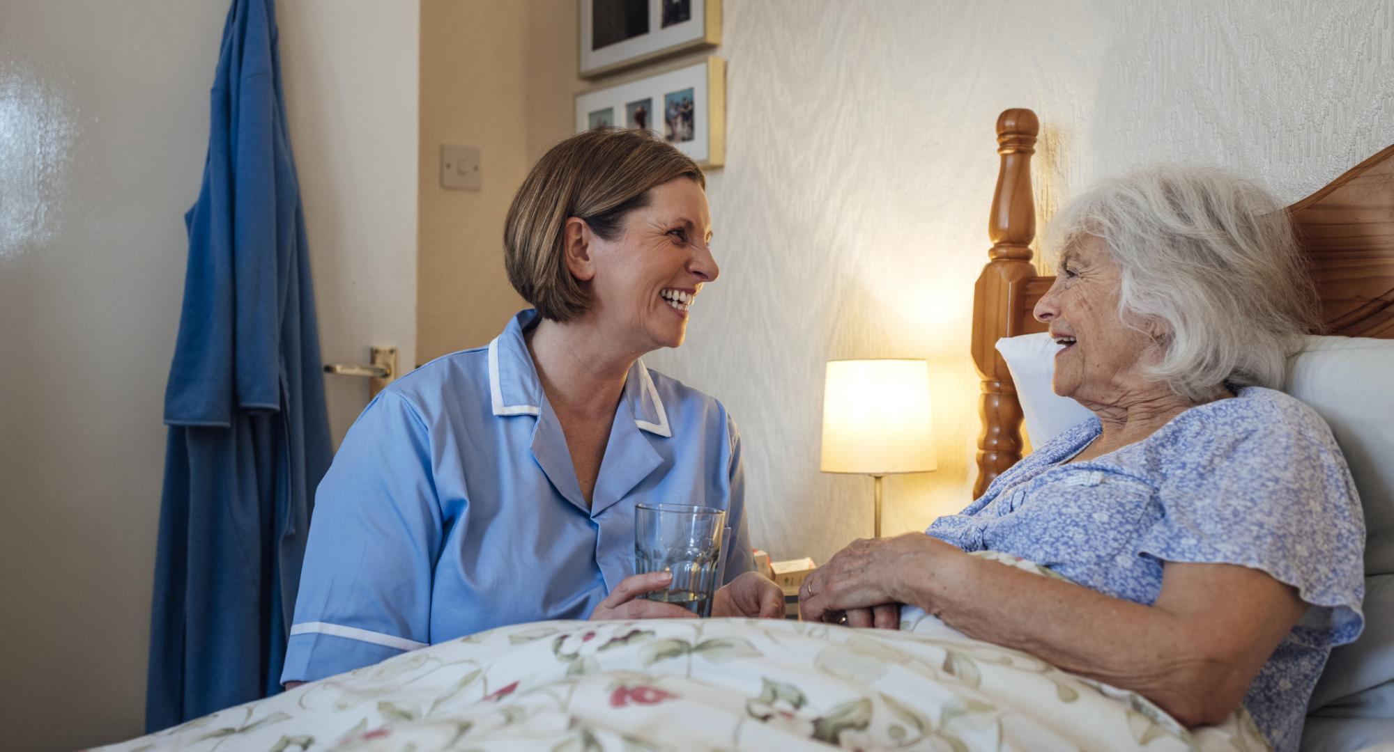 Senior woman lying in bed being helped by a home carer