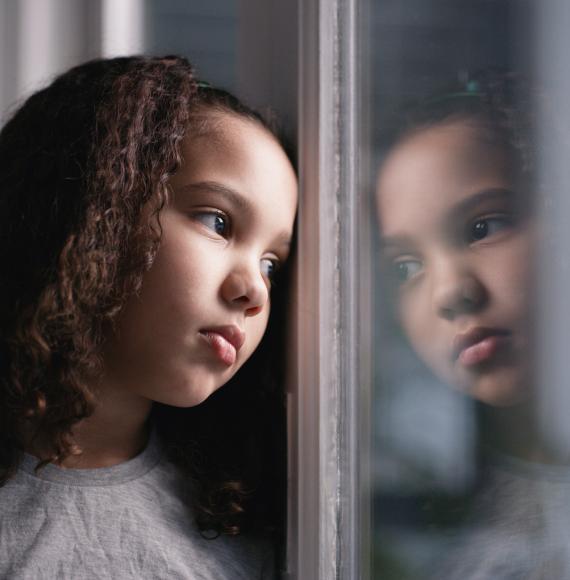 A sad girl looks through a window