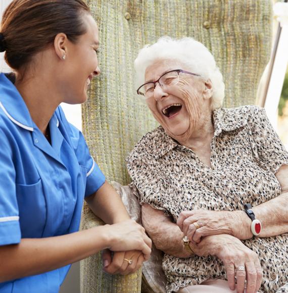 Senior Woman Sitting In Chair And Laughing With Nurse