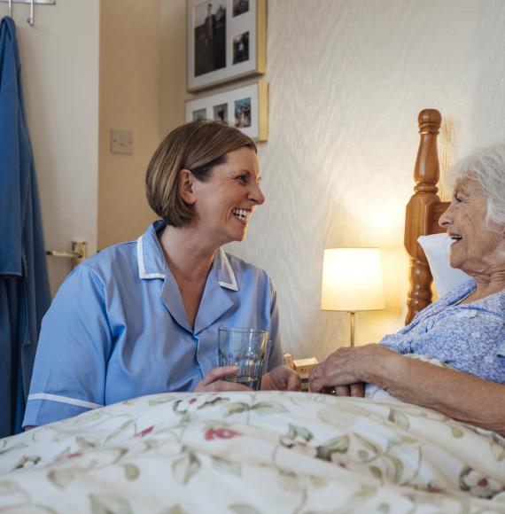 Senior woman lying in bed being helped by a home carer